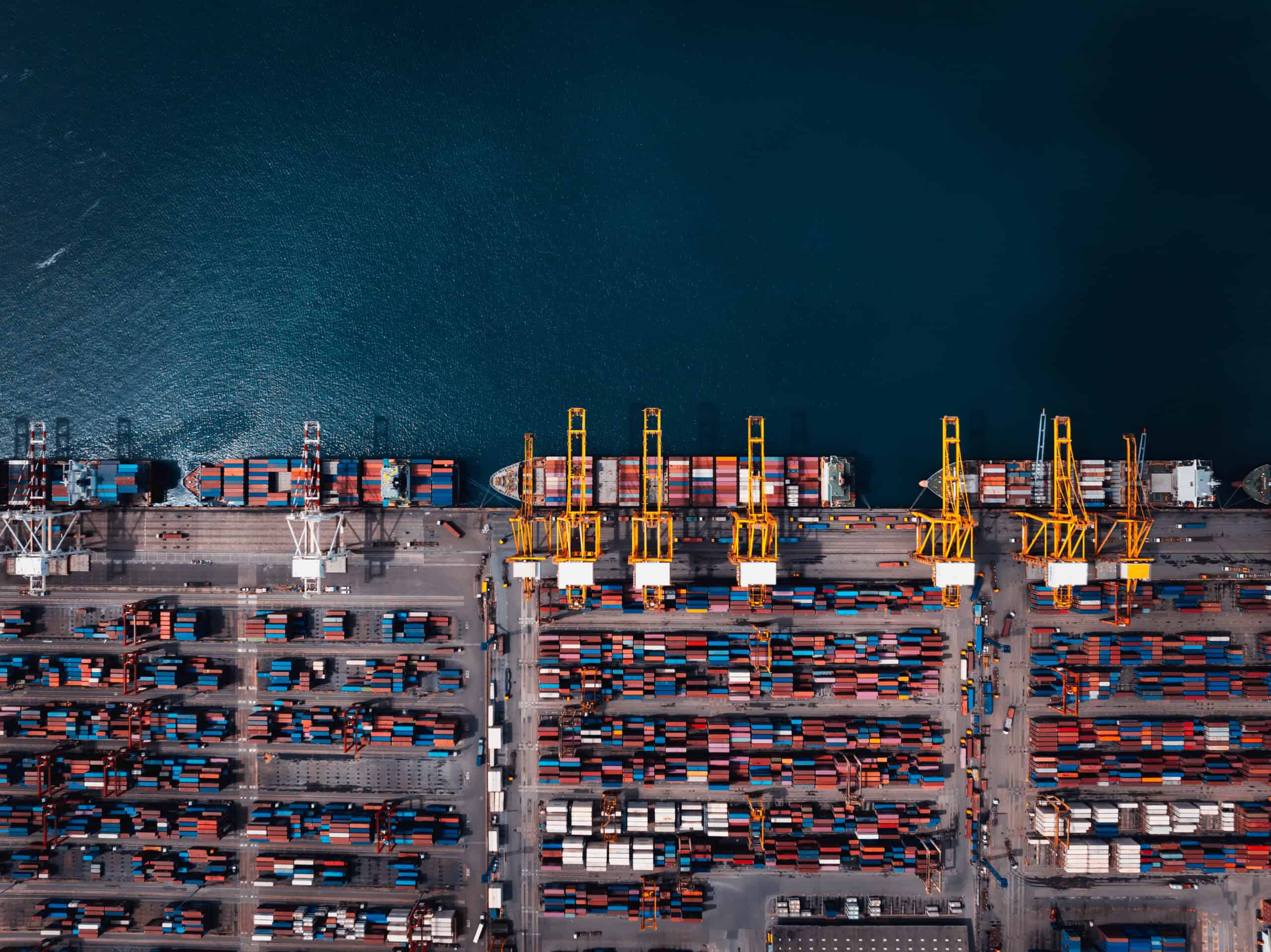 container ship and commercial port in deep sea load and unloading cargo from container ship import and export by crane for distributing goods by logistic trailers transportation. aerial top view cinematic process.