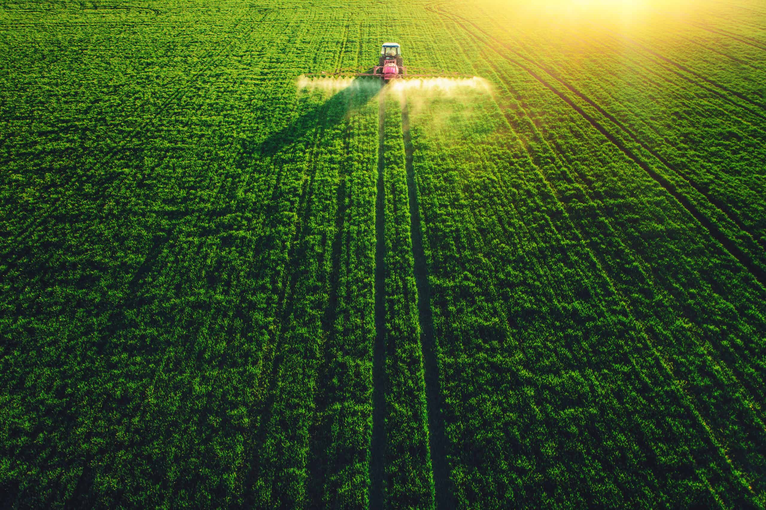 Aerial view of farming tractor plowing and spraying on field.